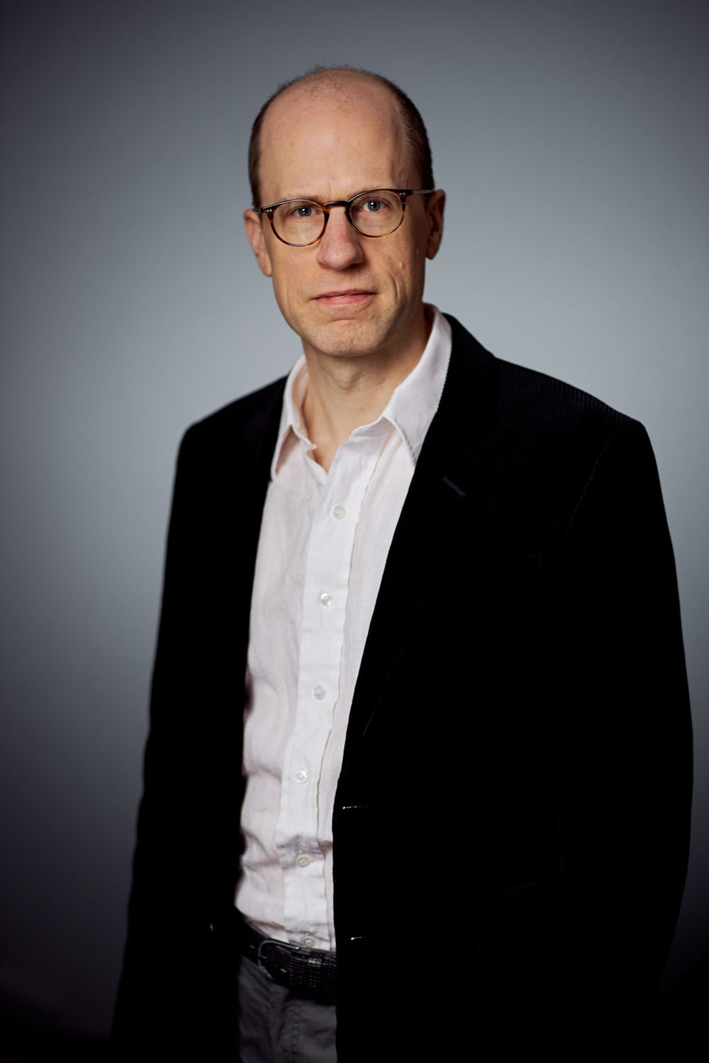 Half-figure portrait of Nick Bostrom with a studio backdrop, wearing a white shirt and black jacket