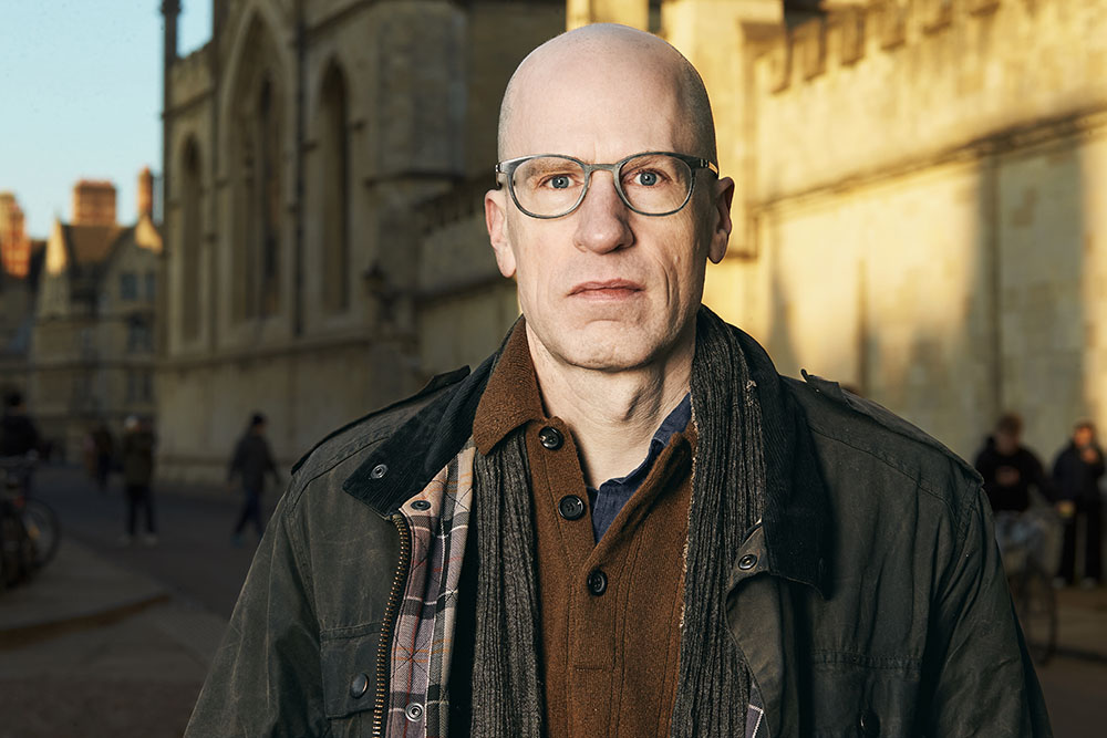 Outdoors half-figure portrait of Nick Bostrom in autumn-coloured clothes in front of an old building in the daytime