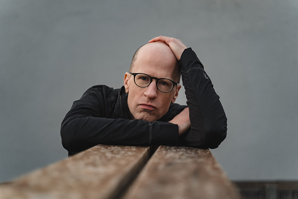 Portrait of Nick Bostrom leaning on a wooden structure